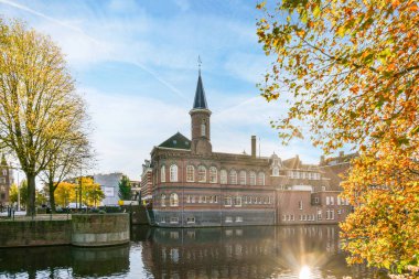 Nehrin kenarındaki eski tuğla bina. Önünde sonbahar yaprakları, altında da mavi gökyüzü var.