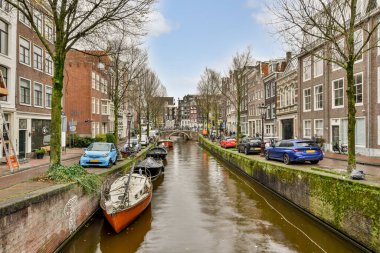 Amsterdam, Hollanda - 10 Nisan 2021: Her iki tarafında tekneler ve binalar olan bir kanal, hepsi birbirine karşı dizilmiş durumda.