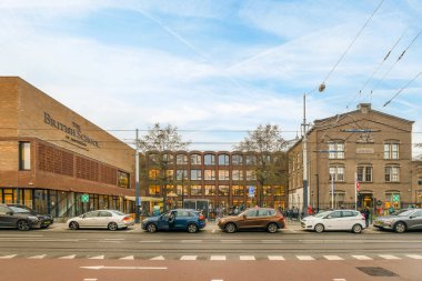 Amsterdam, Hollanda - 10 Nisan 2021: Kenarında arabalar olan bir şehir caddesi ve binaların önünde yürüyen insanlar bir kavşak boyunca