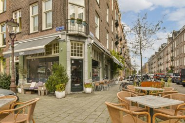 Amsterdam, Hollanda - 10 Nisan 2021: Sokağın kenarına park edilmiş arabalı bir binanın önündeki kaldırımda bazı masa ve sandalyeler