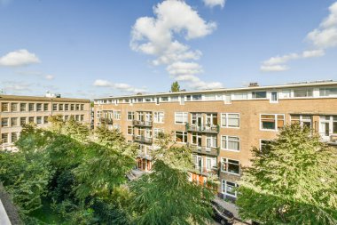 Amsterdam, Hollanda - 10 Nisan 2021: Güneşli bir günde, bir kentsel alanda, üzerinde ağaçlar ve bulutlar olan bazı binalar