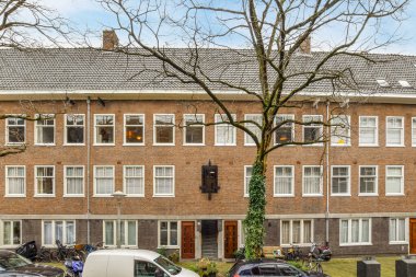 Amsterdam, Hollanda - 10 Nisan 2021: Otoparkın yanına park edilmiş bir apartman ve sokağın iki tarafında da ağaçlar var.