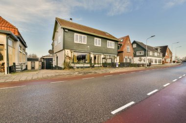 Arka planda evleri olan boş bir cadde ve güneşli bir günde tepesinde kabarık beyaz bulutlar olan mavi bir gökyüzü.