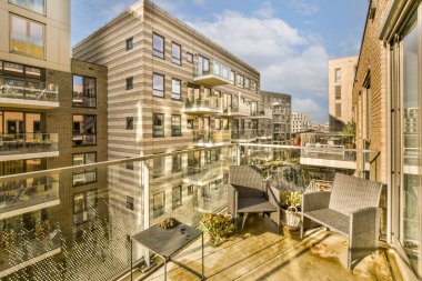 Sokağın karşısındaki bazı binaların önünde sandalyeler, masalar ve şemsiyelerle dolu bir balkon.