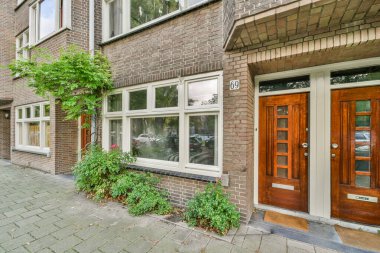 Amsterdam, Hollanda - 10 Nisan 2021: Kapılarında ve kaldırımlarında bazı bitkiler büyüyen tuğla bir bina var.