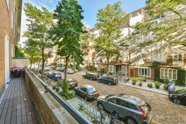 stock image Amsterdam, Netherlands - 10 April, 2021: an empty street with parked cars and trees on either side of the street there is a brick building in the background