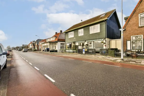 stock image a street with houses and cars parked on the side, in front of it is a blue sky filled with white clouds