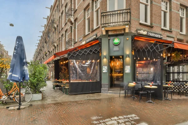 stock image a restaurant in the middle of an urban area with people sitting at tables, chairs and umbrellas on either side of the street