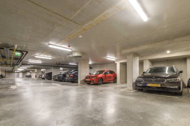 Bir yeraltı otoparkı. Arabalar park halinde ve insanlar arabalarının anahtarlarını almak için kaldırımda yürüyorlar.