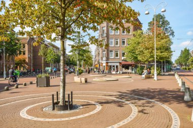 Amsterdam, Hollanda - 10 Nisan 2021: Bir şehir meydanının ortasında ağaçların altındaki banklarda yürüyen ve oturan bir ağaç