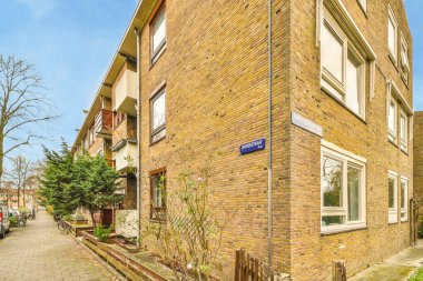 Amsterdam, Hollanda - 10 Nisan 2021: Önünde arabalar ve kaldırım boyunca büyüyen ağaçlar olan bir caddenin kenarındaki tuğla bina