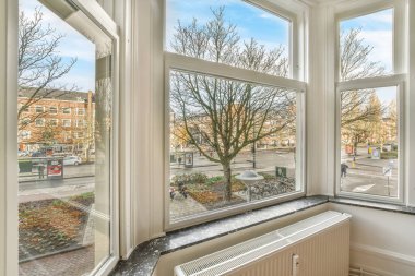 Güneşli bir günde arka planda ağaçlar ve binalar olan bir pencereden dışarıdan bakıldığında,