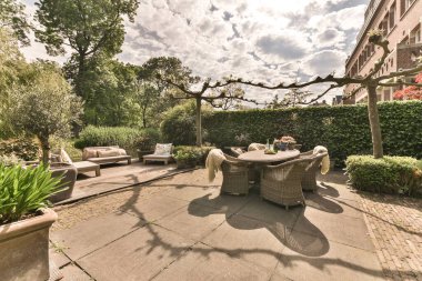 Ortasında sandalyeler ve masalar olan, sokağın her iki tarafında ağaçlar ve çalılarla çevrili bir teras.