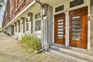 Amsterdam, Hollanda - 10 Nisan 2021: Önünde iki ahşap kapı ve binanın diğer tarafında bir kırmızı kapı olan tuğlalı bir bina