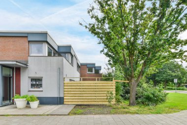 Güneşli bir günde, ön bahçesinde ağaç ve arka kapıya çıkan merdivenleri olan bir ev.