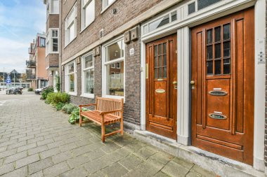 Amsterdam, Hollanda - 10 Nisan 2021: Kapı ve pencerelerinde beyaz süslemeler olan tuğla bir binanın önündeki ahşap bank