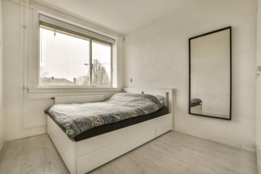 Yatak odası, yatak odası ve pencerenin yanındaki duvarda büyük bir ayna sokağa bakıyor.