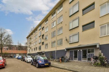 Bir apartmanın önünde yol kenarına park etmiş bir sürü penceresi ve kepenkleri olan birkaç araba var.
