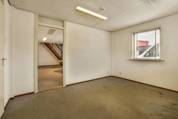 stock image an empty room with white walls and carpet on the floor there is a small window in the wall to the right