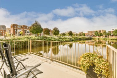 Suya bakan sandalyeli bir balkon ve fotoğrafta her iki taraftaki binalar dışarıdan çekiliyor.