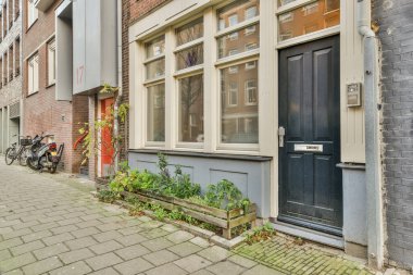 Amsterdam, Hollanda - 10 Nisan 2021: kaldırıma parketmiş bisikletli bir tuğla bina önünde açık bir kapı ve iki pencerenin yanında