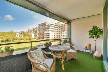 Sandalyeli, masalı bir balkon ve apartman pencerelerinin önündeki çimlerin üzerine bir bitki.