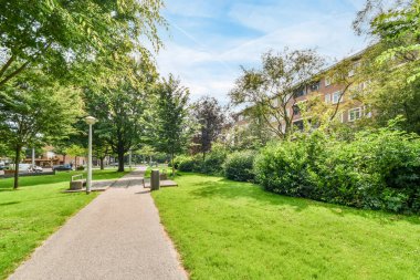 Amsterdam, Hollanda - 10 Nisan 2021: Her iki tarafında yeşil çimenler ve ağaçlar olan yerleşim alanının ortasında boş bir kaldırım var.