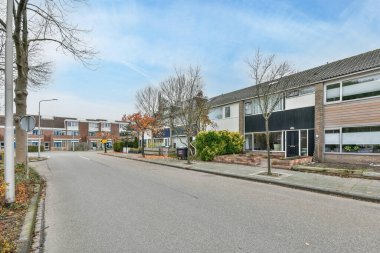 Arka planda evleri ve yolun her iki tarafında da ağaçları olan boş bir cadde var.