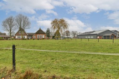 Uzakta bazı evler ağaçlar ve çitlerin diğer tarafında sağda çitlerle çevrili.