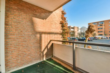 Duvarı tuğlalı ve yeşil çimenleri olan bir dış alan. Otoparka açılan beyaz kapının yanında.