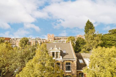 Bazı binalar ön planda ağaçlar ve üzerlerinde mavi gökyüzü, bir apartman balkonundan görüldüğü gibi.