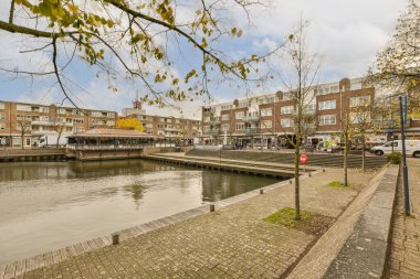 Amsterdam, Hollanda - 10 Nisan 2021: her iki yakasında binalar ve ağaçlar olan bir nehir, suyun karşısından görüldüğü gibi.
