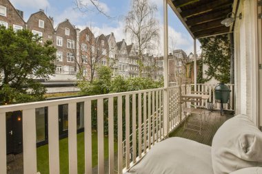 Arka planda ağaçlar ve binalar olan bir balkon. Bir apartmanın penceresinden sokağa bakıyor.