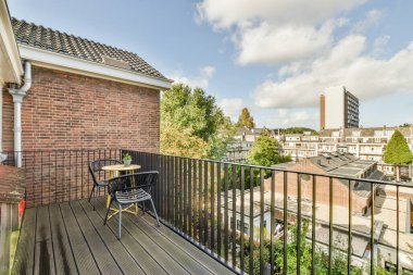 Amsterdam, Hollanda - 10 Nisan 2021: Sol tarafında sandalye ve masa olan bir balkon, sağdaki tırabzandan şehre bakıyor.