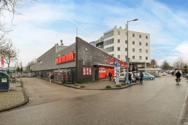 Önünde arabalar olan bir binanın dışında ve insanlar binanın her iki tarafında da caddeden aşağı doğru yürüyorlar.