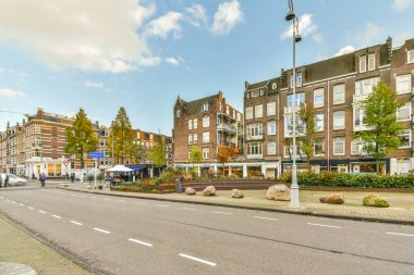 Amsterdam, Hollanda - 10 Nisan 2021: Arka planda binalar ve kaldırımda yürüyen insanlar olan bir şehir sokağı, yoldan geçen bazı arabalar