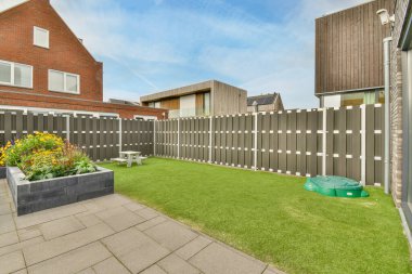 Amsterdam, Hollanda - 10 Nisan 2021: Bahçesinde bazı bitkiler ve çiçekler olan bir arka bahçe alanı, ahşap çitlerle çevrili yapay bir çimen de dahil.