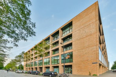 Amsterdam, Hollanda - 10 Nisan 2021: yanında arabaların park ettiği tuğla bir bina ve önünde yürüyen insanlar