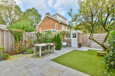 Amsterdam, Hollanda - 10 Nisan 2021: Bahçenin ortasında masa, sandalye ve açık hava yemek seti bulunan bir arka bahçe alanı ağaçlarla çevrilidir.