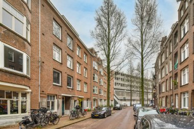 Yolun kenarında park etmiş arabaları ve bisikletleri olan bir şehir caddesi. Birkaç tuğladan binanın önünde.