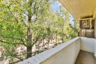 Arka planda ağaçlar ve binalar olan bir balkon. Üst kattaki bir apartmandan alınmış.