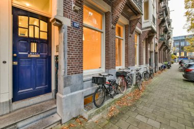 Amsterdam, Hollanda - 10 Nisan 2021: Çevresinde sarı bukle olan mavi bir kapı ve tuğla duvarın önündeki binanın kenarına parketmiş bisikletler