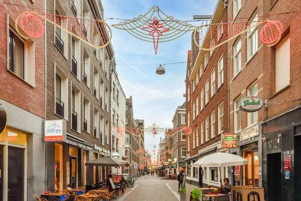 オランダ アムステルダム 2021年4月10日 通りの真ん中にテーブルと傘に座っている人々がいる街の通りには 両側に多くの建物があります — ストック写真