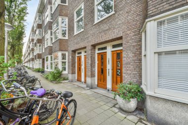 Amsterdam, Hollanda - 10 Nisan 2021: Beyaz kepenkleri ve pencereleri olan tuğla bir binanın önündeki caddenin kenarına parketmiş bisikletler