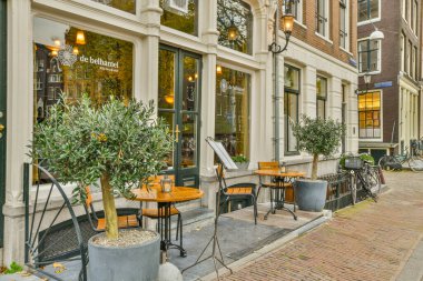Amsterdam, Hollanda - 10 Nisan 2021: tuğladan yapılma binalarla dolu bir caddede bir mağaza önü önünde masa ve sandalyelerle dolu bir kaldırım