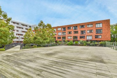 Ön planda ağaçlar ve binanın yanında boş bir bank olan bazı binalar kırmızı tuğladır.