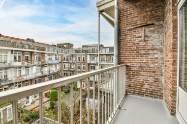 Amsterdam, Hollanda - 10 Nisan 2021: Sol tarafında tuğla duvarlar ve çıkıntılar olan bir balkon, arka planda mavi bir gökyüzü var.