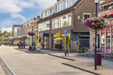 Amsterdam, Hollanda - 10 Nisan 2021: kaldırımlarda yürüyen ve dükkanların, restoranların önünde park etmiş arabaların olduğu bir şehir caddesi