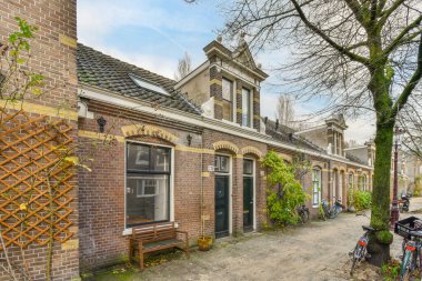 Kaldırımda bisikletleri olan eski bir ev ve önünde yaprakları olmayan bir ağaç var.