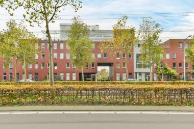 Amsterdam, Hollanda - 10 Nisan 2021: Önünde ağaçlar ve sokağın diğer tarafında çalılar olan bir apartman.